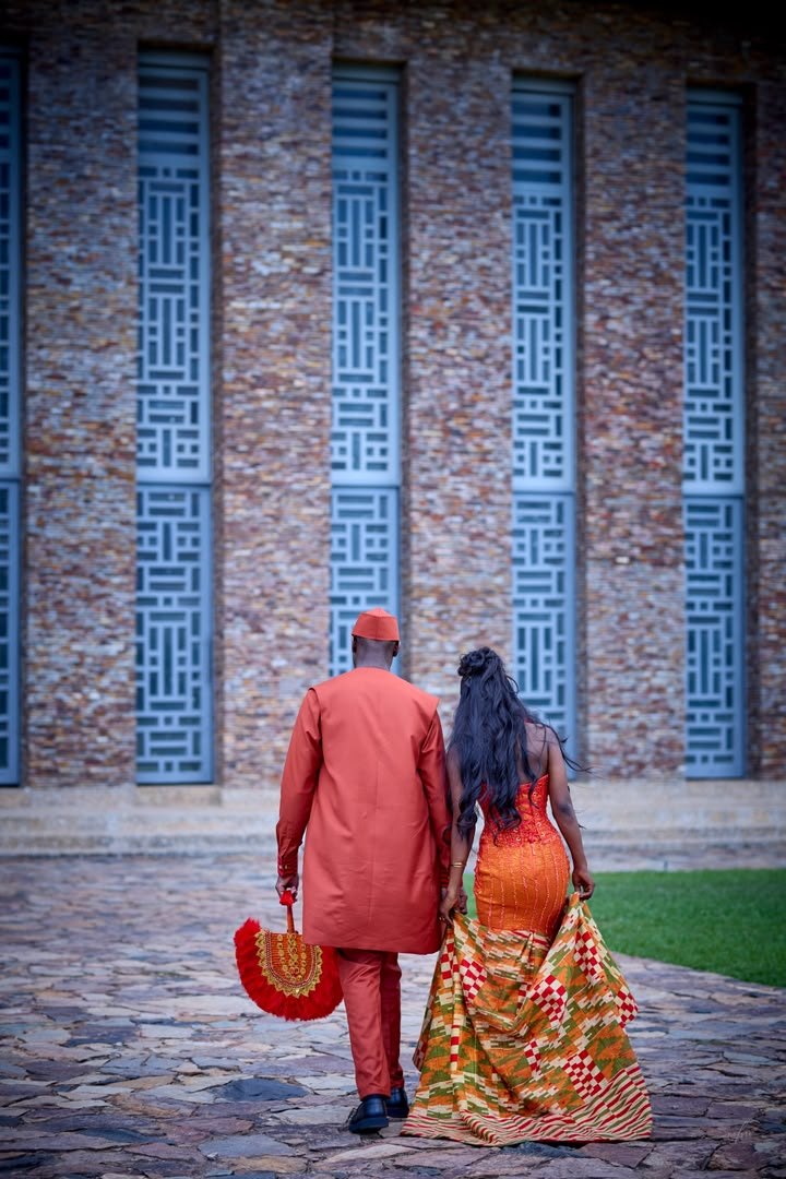 Asomdwe and Richard walking together, her kente train trailing behind